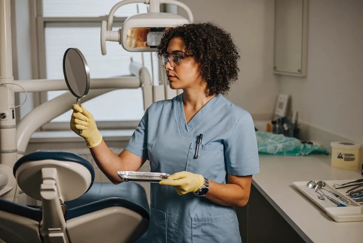 A dental hygienist holding a mirror and instrument tray beside a dental exam chair